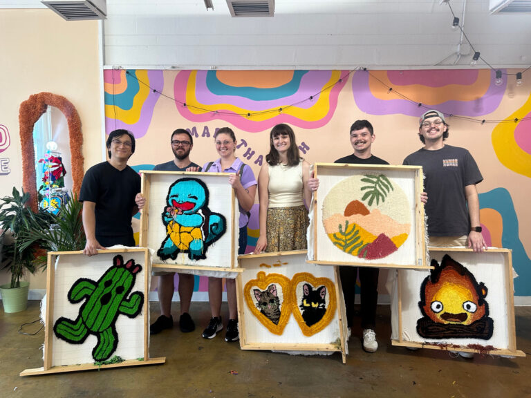 Group holding finished tufted rugs in the studio